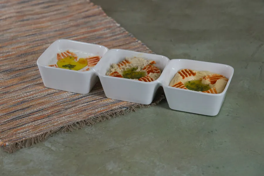 Three white dishes of hummus with olive oil and paprika