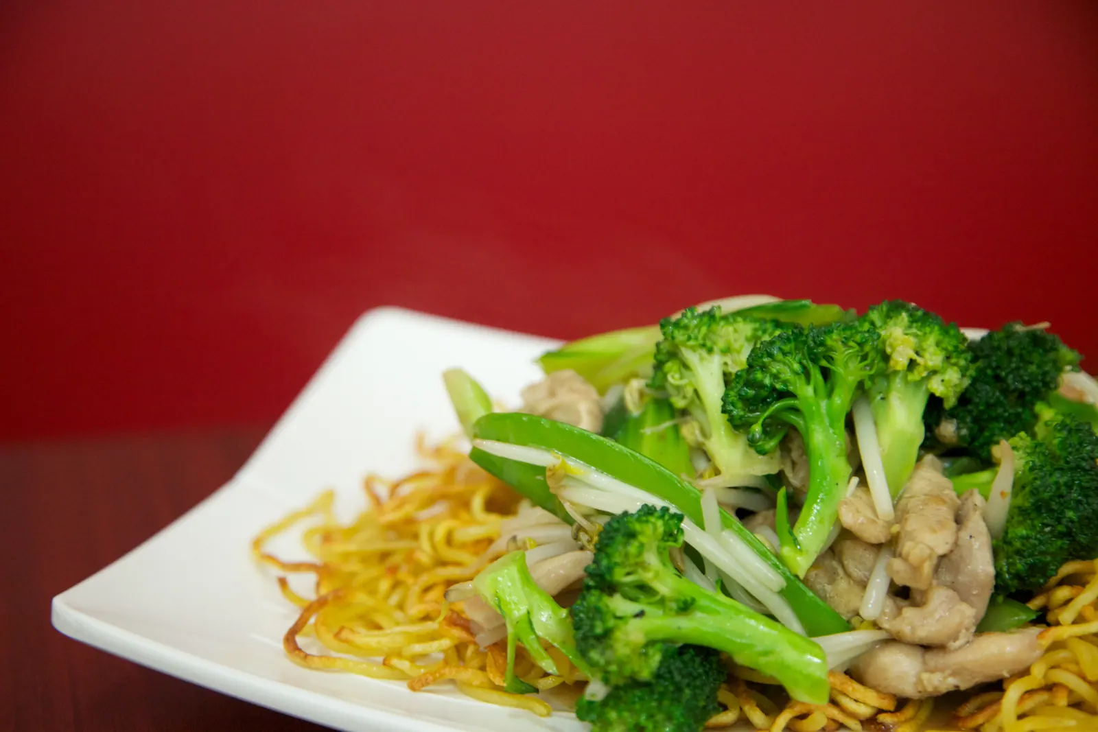 Noodles with broccoli and chicken on a square white plate