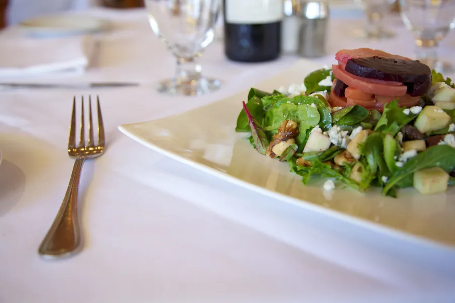 Plated salad on a set table with water glasses and a wine bottle