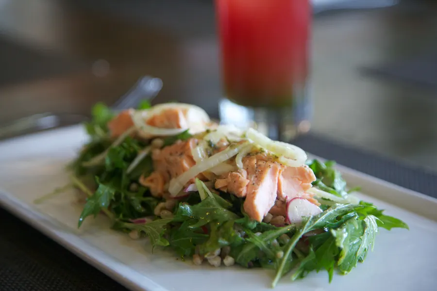 Salmon and grain salad on a white plate with a red drink behind it