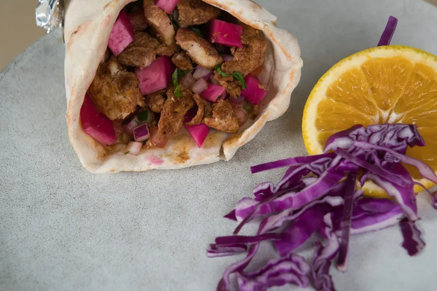 Chicken shawarma wrap with pickled turnips, half an orange and red cabbage