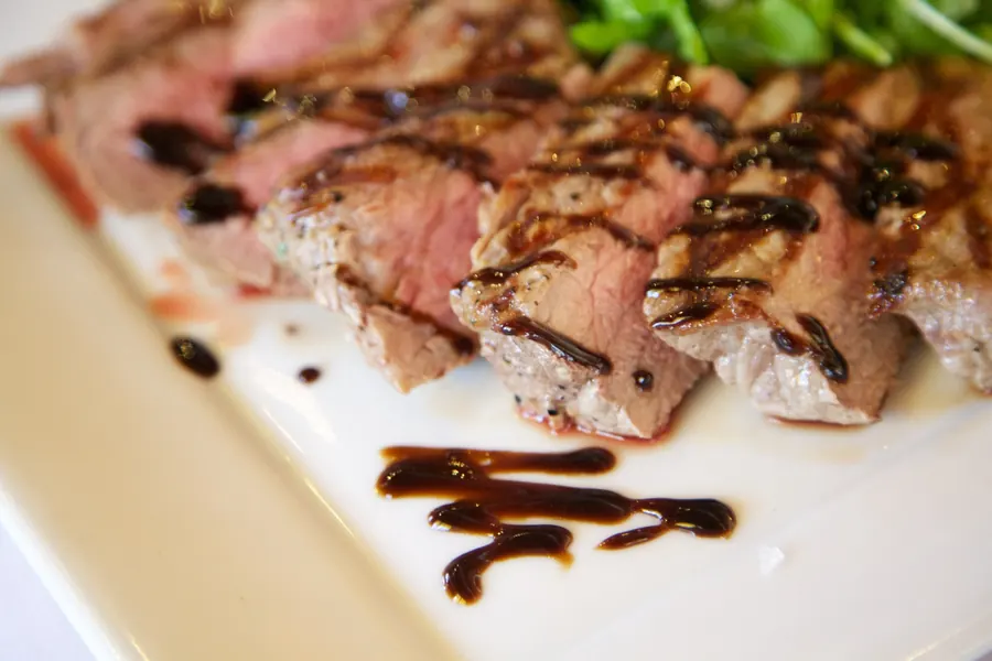 Sliced seared steak with a balsamic drizzle on a square white plate