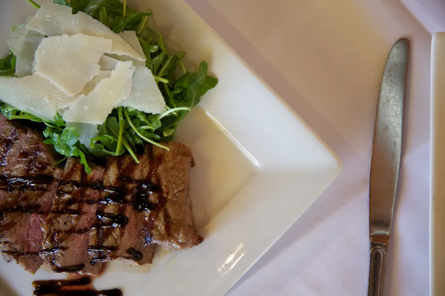 Seared steak with shaved cheese and arugula on a square plate