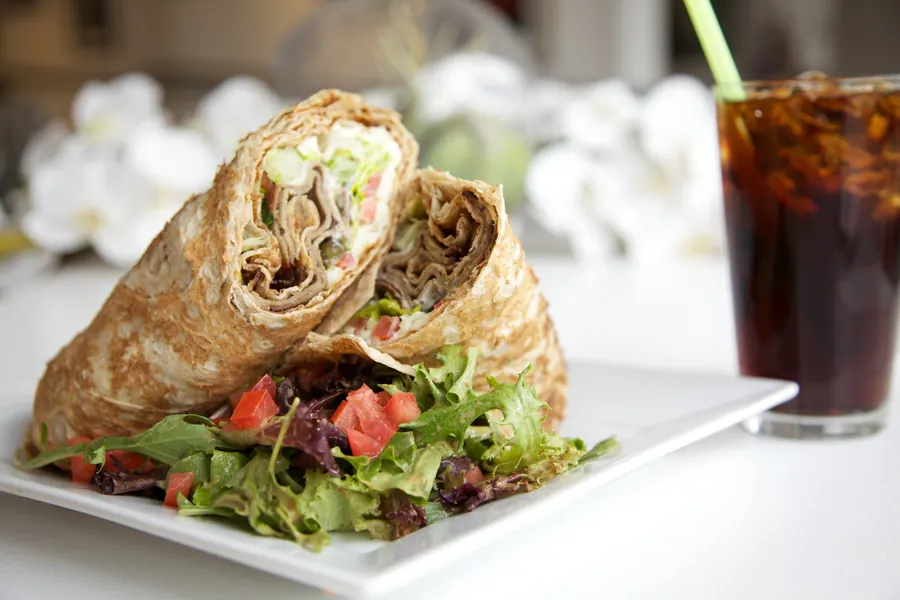 Wrap cut in half beside a green salad and a glass of cola