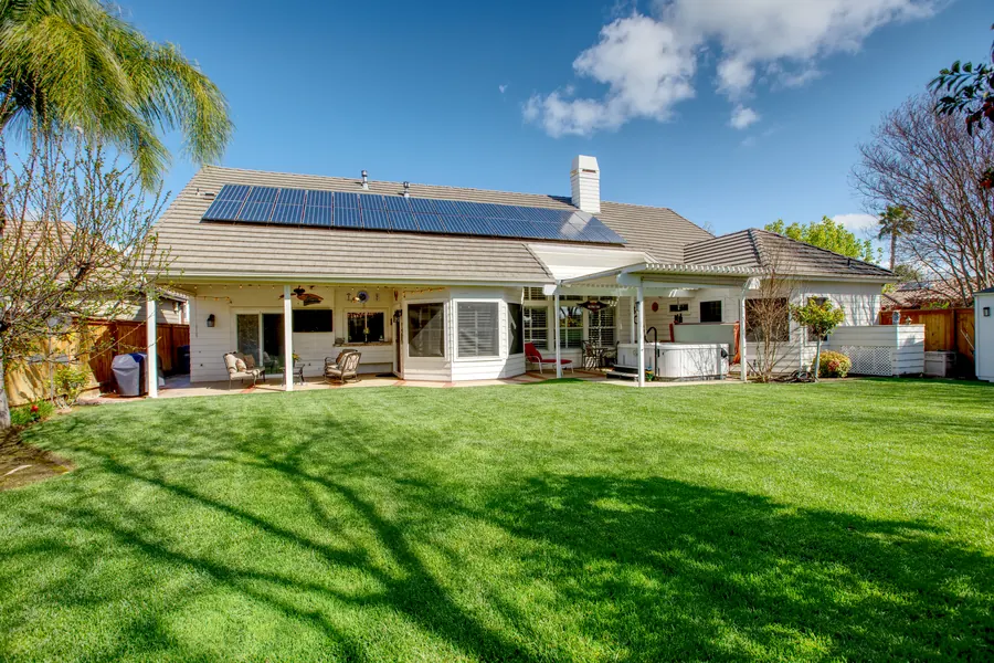 Single-story home with solar panels and a green backyard lawn