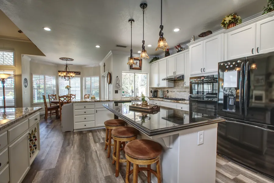 Home kitchen with white cabinets and a white island with a dark granite top and bar stools