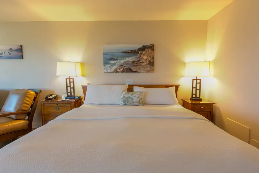 Hotel room bed with a framed coastal painting between two lamps