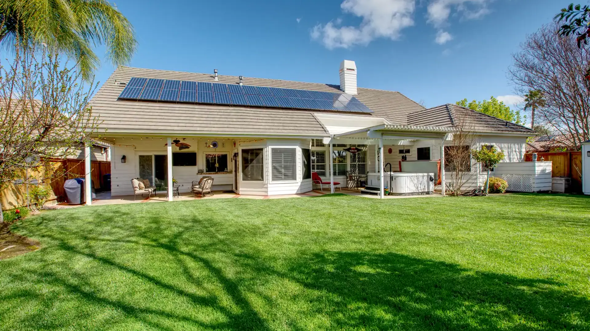 Single-story home with solar panels and a green backyard lawn